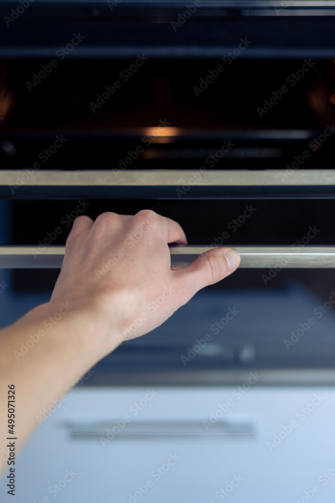 The hand opens the oven door. 
