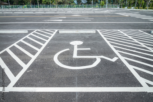 Wheelchair handicap sign at outdoor asphalt car parking lot in public green park sunny day.