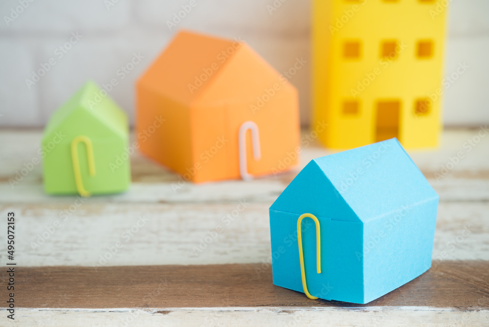 Fototapeta premium Colorful paper house on wooden table background with free copy space. Home loan, mortgage, real estate property or construction concept.