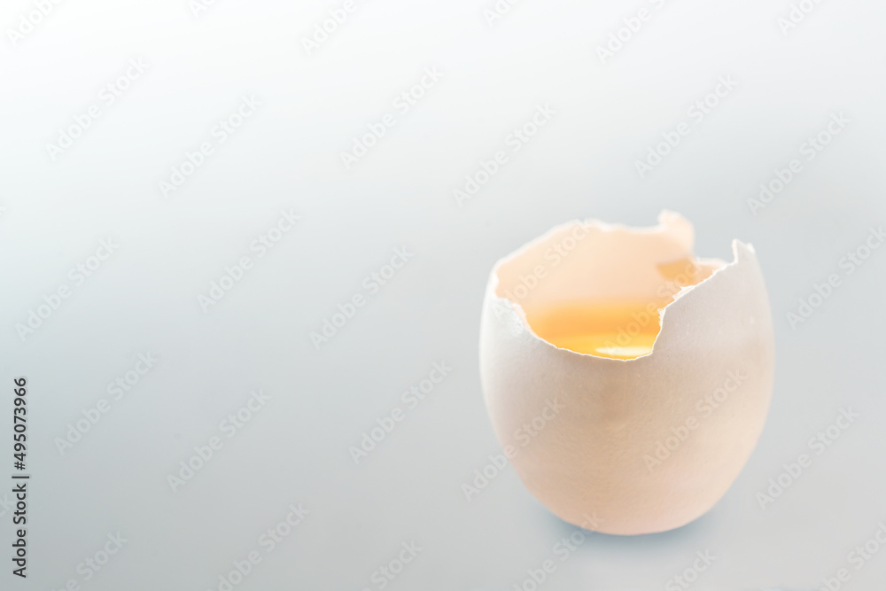 Cracked white egg with yellow yolk on a light gray background, copy space, selected soft focus Cracked white egg with yellow yolk on a light gray background, copy space, selected soft focus