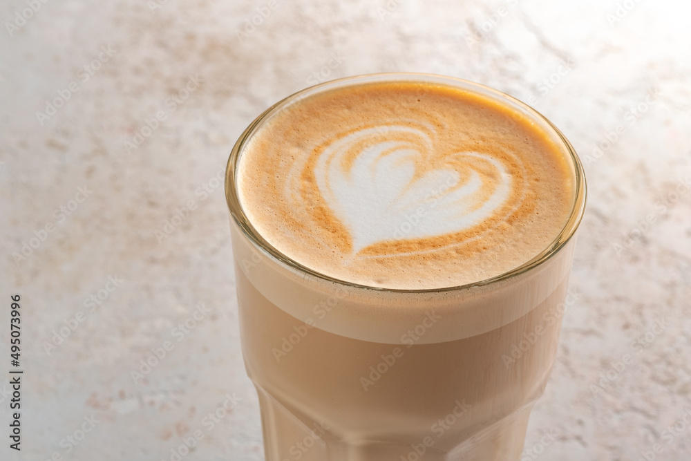 A glass of cappuccino or latte with foam and a heart pattern on a stone white table. Coffee mug minimalist style, closeup and text space A glass of cappuccino or latte with foam and a heart pattern on a stone white table. Coffee mug minimalist style, closeup and text space