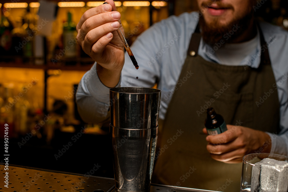 hand of male bartender drips the ingredient into the shaker cup