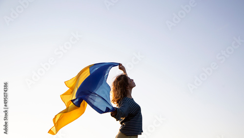 sunset, a woman's silhouette holds behind her back the Ukrainian flag fluttering in the wind. Ukrainians against the war. Drawing attention to military actions in Ukraine