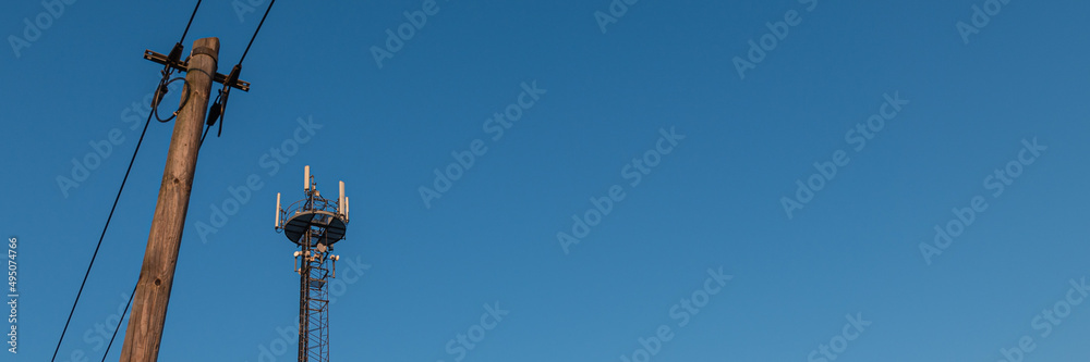 Obraz premium Mobilfunkmast und Mast mit Leitung vor blauem Himmel