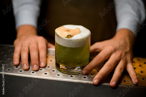 glass with a bright green foamy cocktail decorated with slice of dry apple