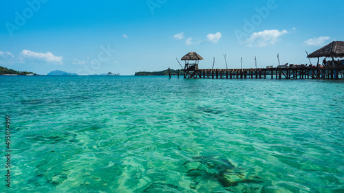 Koh Mak Island, Trat, Thailand. Scenic view of peaceful sea, crystal clear turquoise water with coral reef transparent and long wooden pier bridge landmark against blue sky in summer.