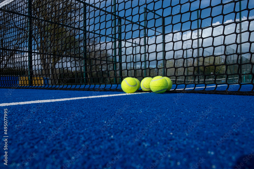 selective focus, five paddle tennis balls near the net of a blue paddle tennis court