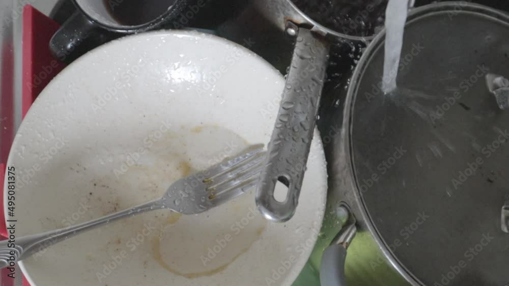 The kitchen utensils in the wash basin need to be washed. A pile of dirty dishes in the kitchen sink with running water. Kitchen utensils need washing. Homework concept. The kitchen utensils in the wash basin need to be washed. A pile of dirty dishes in the kitchen sink with running water. Kitchen utensils need washing. Homework concept.