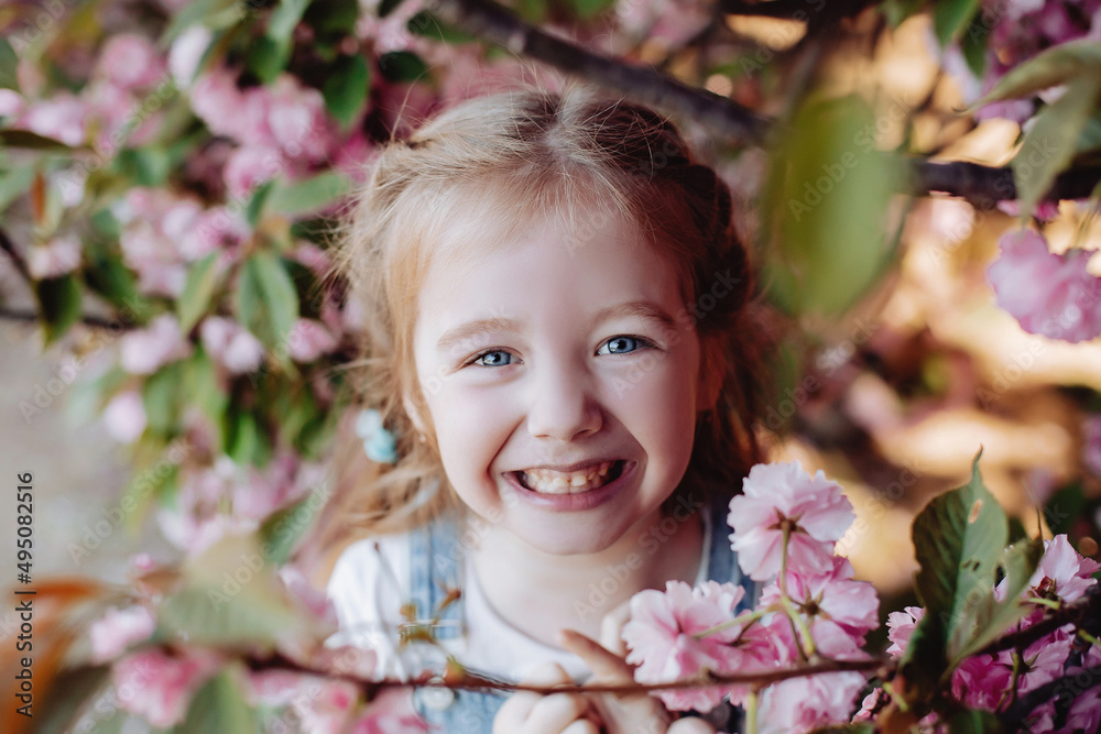 Close up of beautiful red-haired girl sincerely smiling in the park near sakura.