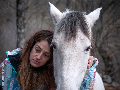 Brunette female with a sad, melancholic look on her face and her white horse on a winter day.