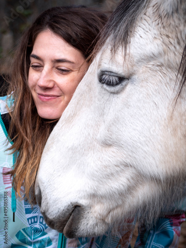 Horizontal view of brunette female smiling and showing complicity with her white horse.