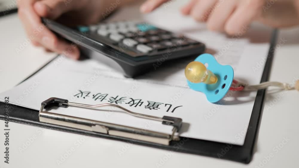 Agreement on the adoption of child in Chinese-speaking language. The hands of lawyer or parents calculate the cost of buying child on calculator. In the foreground lies baby pacifier. Agreement on the adoption of child in Chinese-speaking language. The hands of lawyer or parents calculate the cost of buying child on calculator. In the foreground lies baby pacifier.