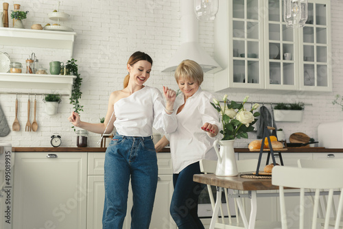 Elderly woman dancing to energetic music with grown up daughter. Happy smiling two generations female family having fun together in kitchen