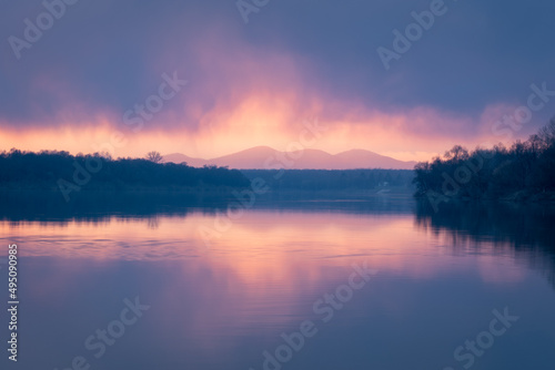 Fototapeta Naklejka Na Ścianę i Meble -  Colorful sunset on Sava river with low clouds and mountain Motajica in bright glowing mist - rural landscape