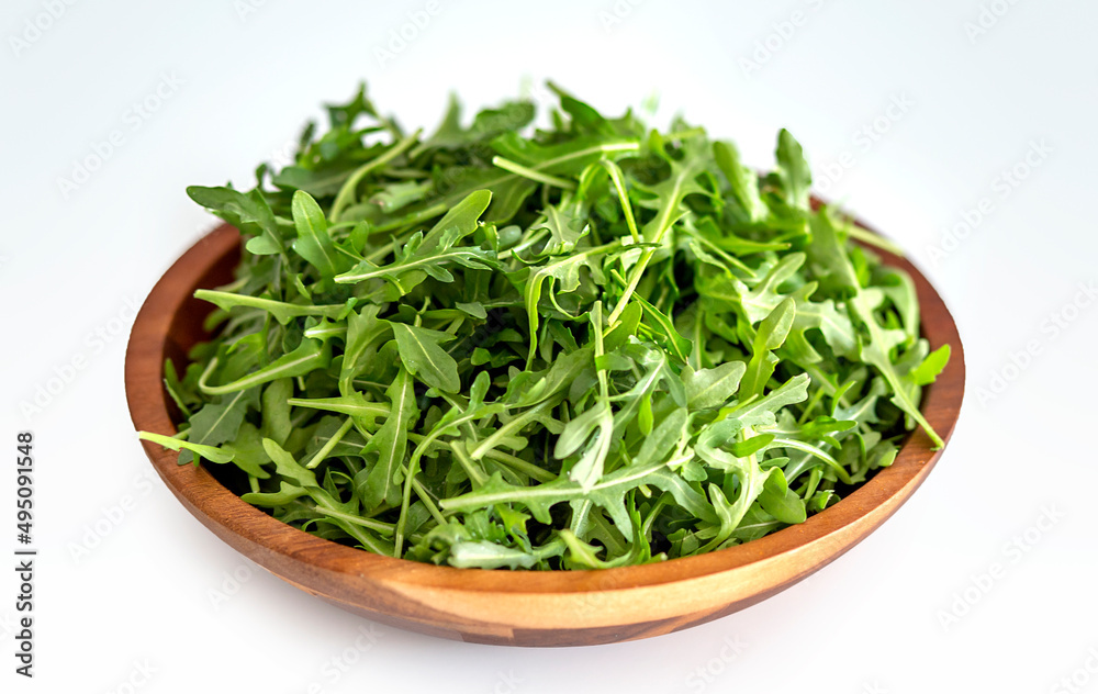 Fresh arugula leaves in wooden bowl on a white background Fresh arugula leaves in wooden bowl on a white background