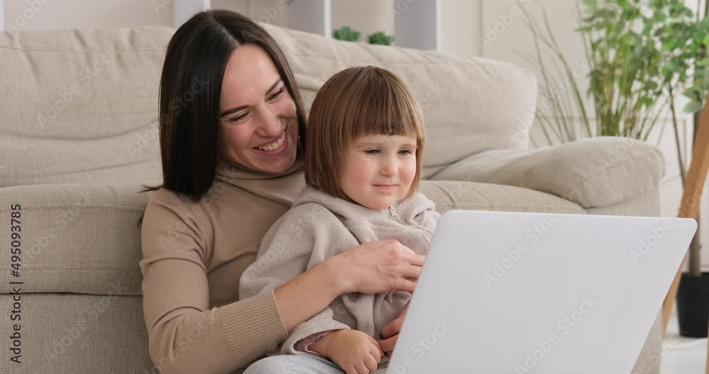 Playful mother tickling daughter while using laptop at home Playful mother tickling daughter while using laptop at home