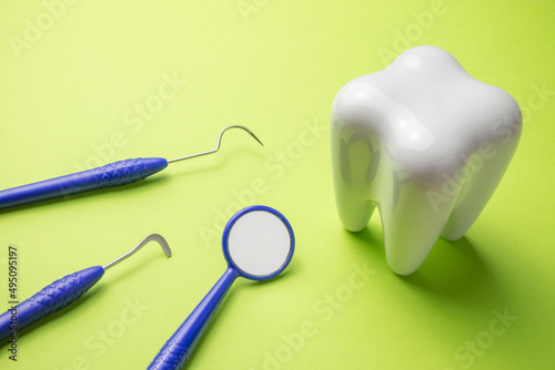 White tooth with sickle scaler and small mirror on green background. Dental care concept.
