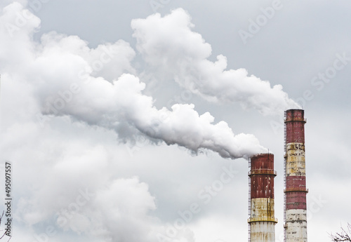 Thick white smoke from industrial factory old rusty chimneys on a cloudy grey sky background photo