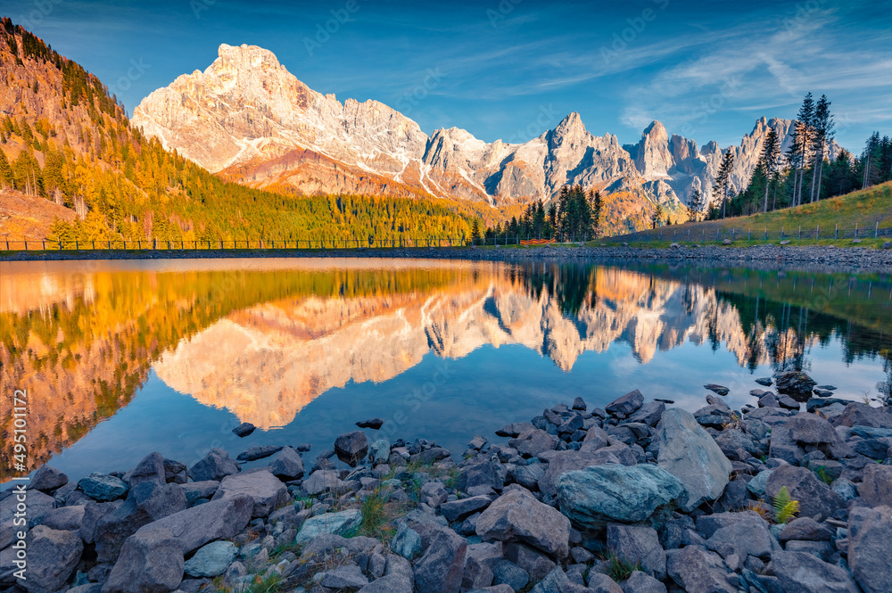 Majestic morning view of Dolomite Alps. Pala di San Martino Mountain Range reflected in the surface of Malga Ces Lake. Gorgeous autumn scene of Italy, Europe. Beauty of nature concept background.