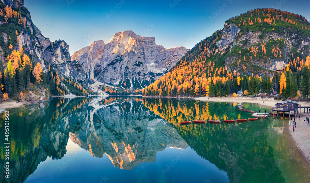 Small chapel on the shore of Braies Lake with recreational boats. Aerial autumn scene from flying drone of Dolomite Alps, Italy, Europe. Beauty of nature concept background.