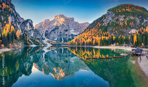 Small chapel on the shore of Braies Lake with recreational boats. Aerial autumn scene from flying drone of Dolomite Alps, Italy, Europe. Beauty of nature concept background.