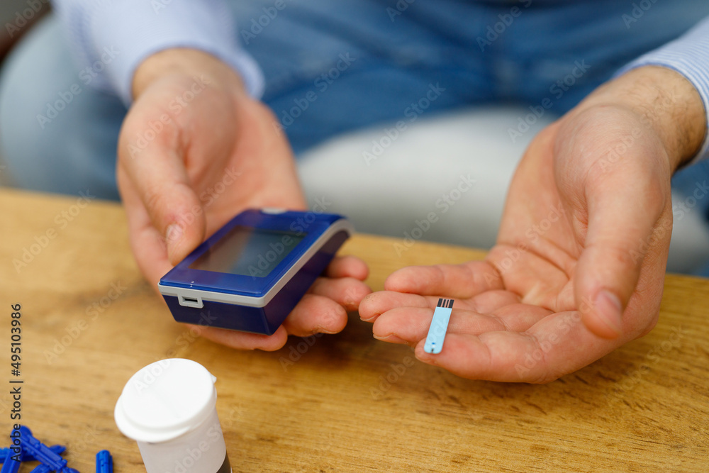 Man sitting at the table holding in his hands glucometer and stripes for checking blood sugar level, diabetes concept. Man sitting at the table holding in his hands glucometer and stripes for checking blood sugar level, diabetes concept.