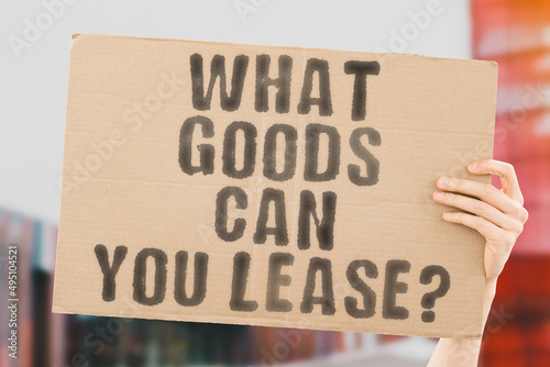 The question "What goods can you lease? " on a banner in men's hands with blurred background. Form. Good. Deal. Interest. Policy. Renting. Resident. Trade. Trust. Vehicle. Law. Property. Rental. Home © AndriiKoval