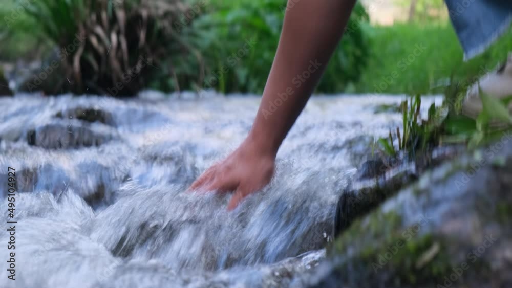 Female hand touching cold water in the river. Trekking woman stands on a rock and touches a stream with her hands. Close-up of the hand Female hand touching cold water in the river. Trekking woman stands on a rock and touches a stream with her hands. Close-up of the hand