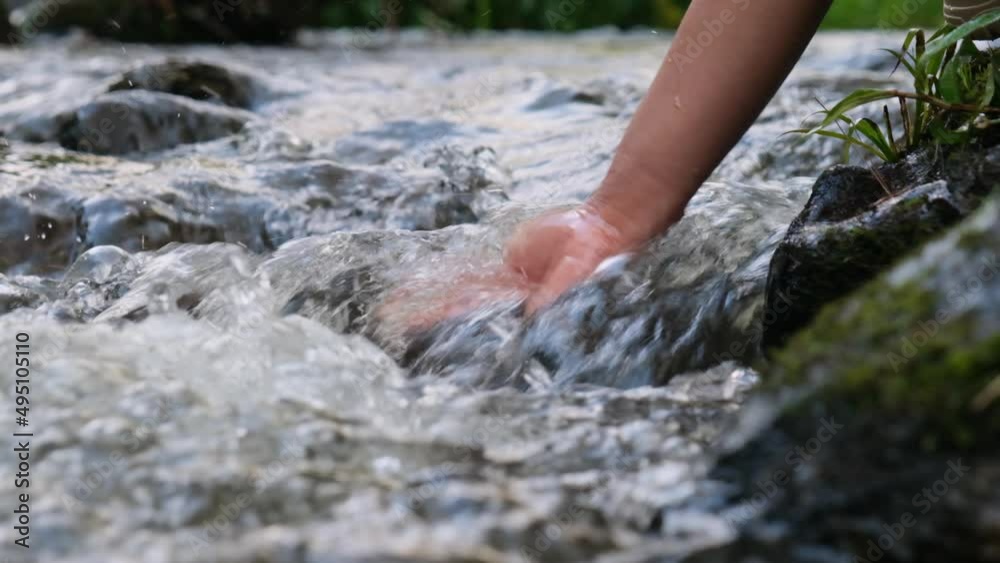 Female hand touching cold water in the river. Trekking woman stands on a rock and touches a stream with her hands. Close-up of the hand Female hand touching cold water in the river. Trekking woman stands on a rock and touches a stream with her hands. Close-up of the hand