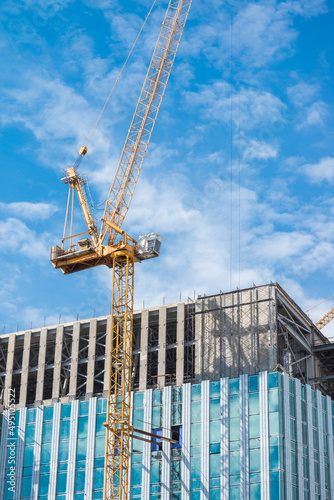 Canvas Print Tower crane in modern office building construction site with blue sky background