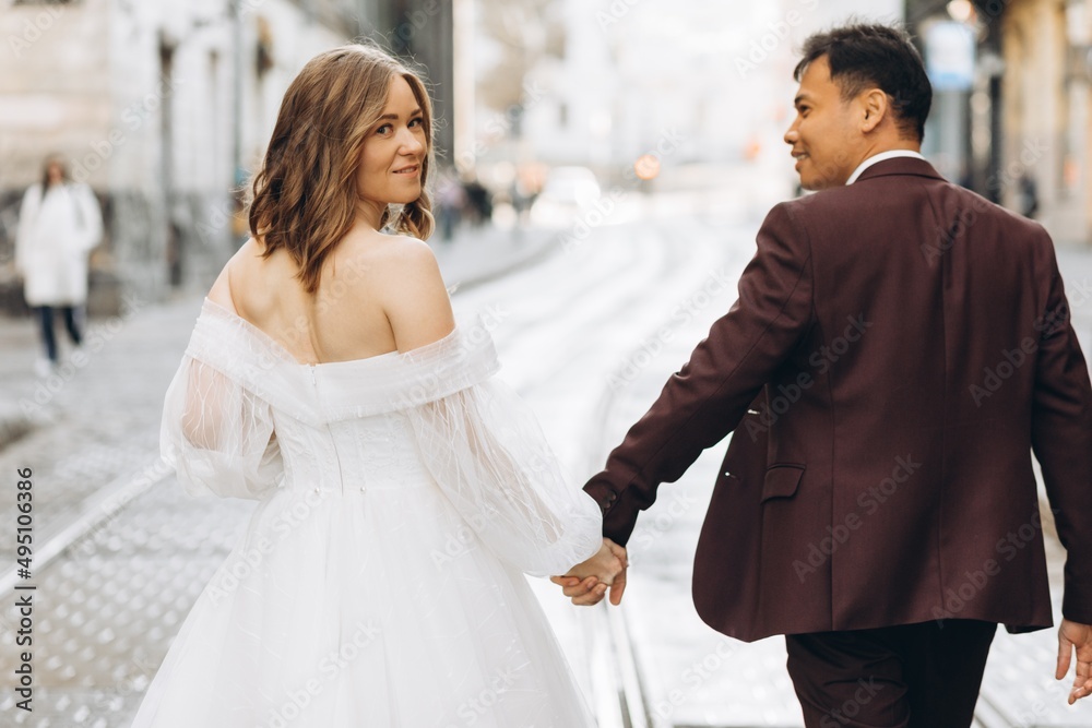 An international wedding couple, a European bride and an Asian groom walk around the city together.