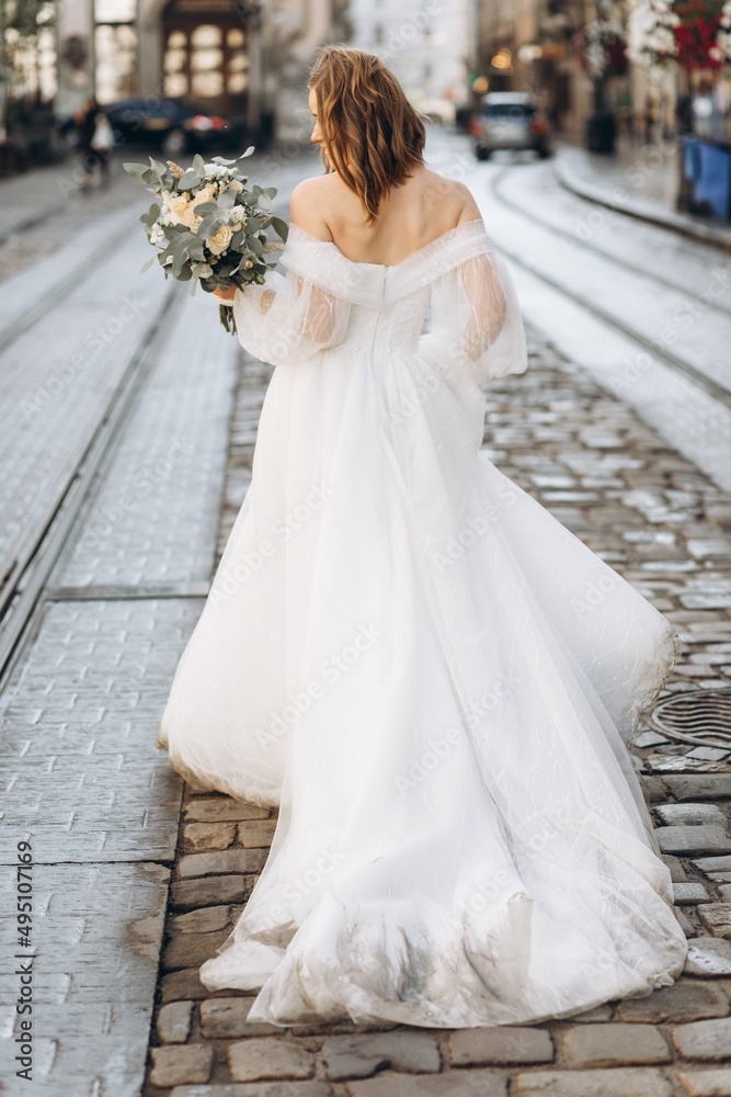 Beautiful bride with a bouquet posing in the city streets