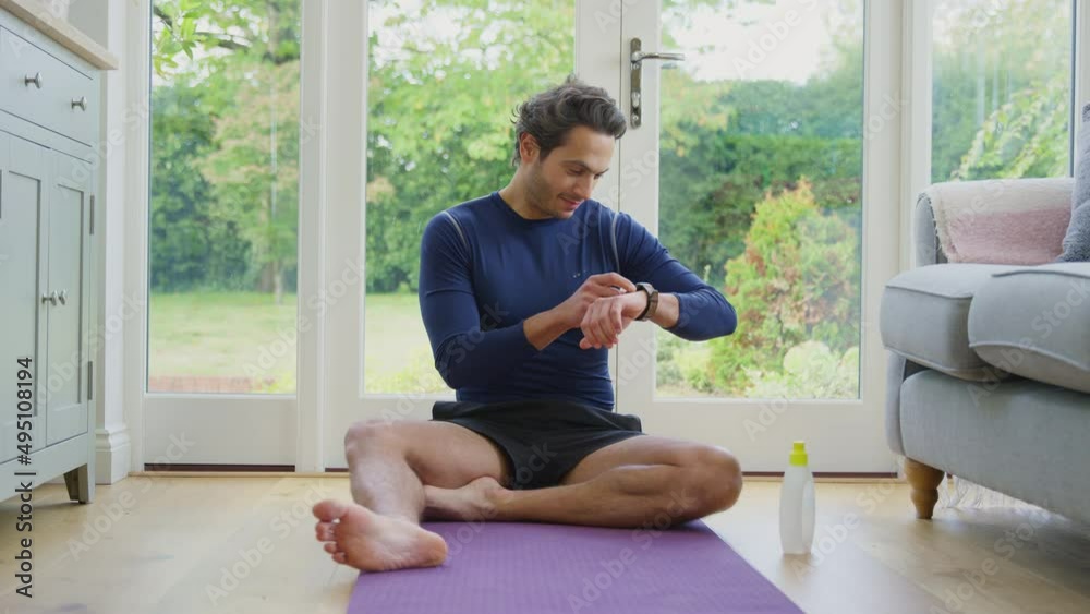 Mature man sitting on yoga mat at home after exercise looking at smart watch - shot in slow motion Mature man sitting on yoga mat at home after exercise looking at smart watch - shot in slow motion