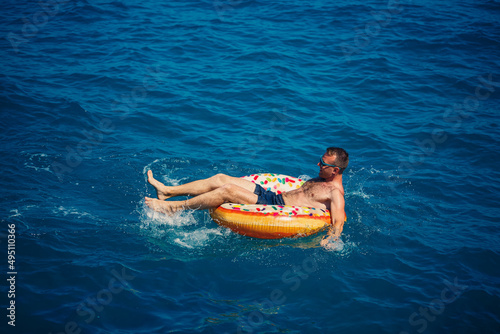 A young man swims in the open sea on an inflatable ring on a sunny day. Summer vacation, tourist on vacation © Дмитрий Ткачук