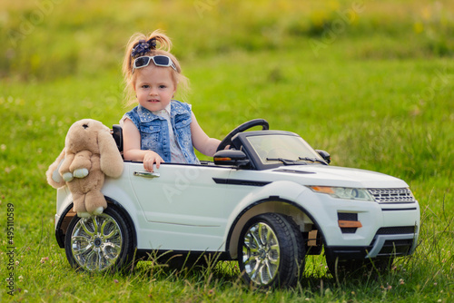 little girl rides on a children's car on a green lawn