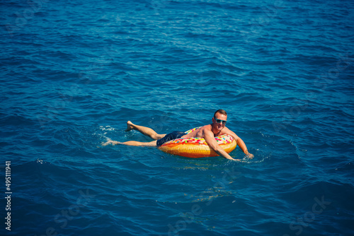 A young man floats on an inflatable air ring circle in the sea with blue water. Festive holiday on a happy sunny day.