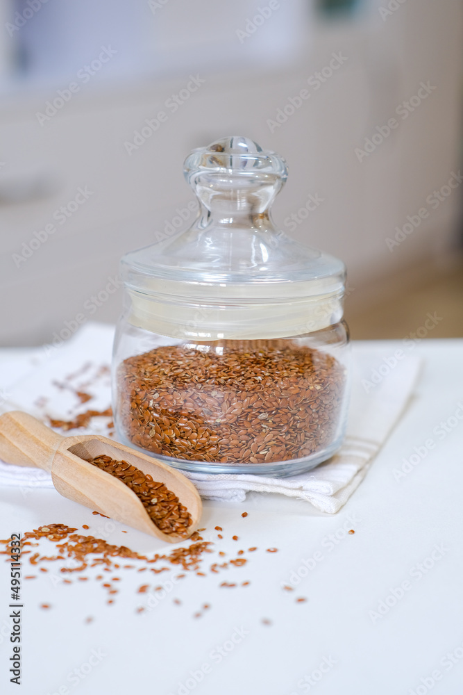 Flax seeds in a glass jar with wooden spoon on a linen napkin in the kitchen. Ingredient for flaxseed porridge and jelly. Minimalistic simple natural light template. Superfood. Organic eco healthcare. Flax seeds in a glass jar with wooden spoon on a linen napkin in the kitchen. Ingredient for flaxseed porridge and jelly. Minimalistic simple natural light template. Superfood. Organic eco healthcare.