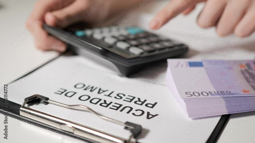 loan agreement in Spanish-speaking languages. The hands of a banker woman calculate the loan terms, repayment terms and monthly payment on a calculator. A woman borrows money, a credit card. loan agreement in Spanish-speaking languages. The hands of a banker woman calculate the loan terms, repayment terms and monthly payment on a calculator. A woman borrows money, a credit card.