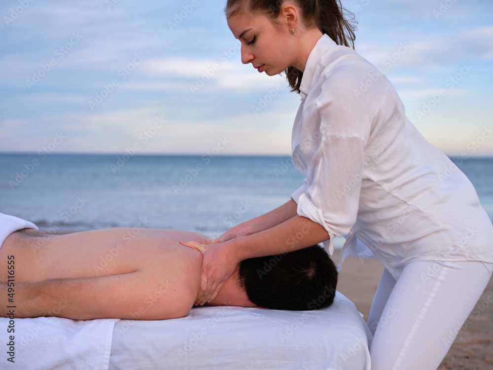 Young chiromassage therapist giving a shoulder massage to young man on a beach in Valencia. Young chiromassage therapist giving a shoulder massage to young man on a beach in Valencia.
