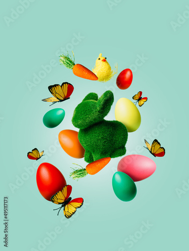 Easter bunny, colorful eggs, chick, butterfly and spring flower flying in the air against pastel green background. Minimal Easter holiday concept. Creative traditional greeting card or banner.