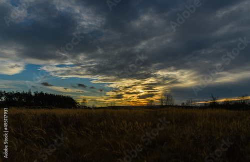 sunset behind clouds over landscape with trees and grass