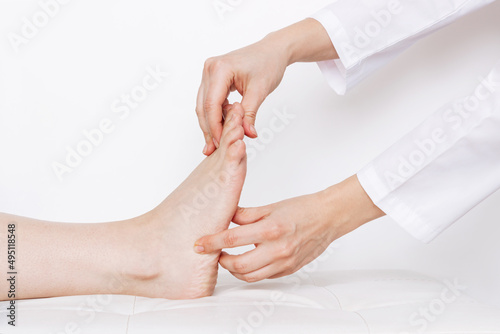 Examination of a young woman by an orthopedist. Cropped shot of female doctor holding a girl's foot in her hands on a white background. Flat feet, injury. Foot treatment. Pain from uncomfortable shoes