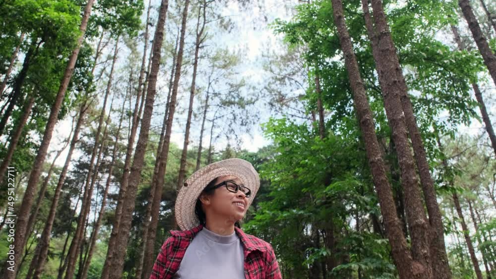 Hipster woman in straw hat and red plaid shirt is walking in a pine alley enjoying nature. Happy Asian female traveler sightseeing in pine tree garden. Hipster woman in straw hat and red plaid shirt is walking in a pine alley enjoying nature. Happy Asian female traveler sightseeing in pine tree garden.