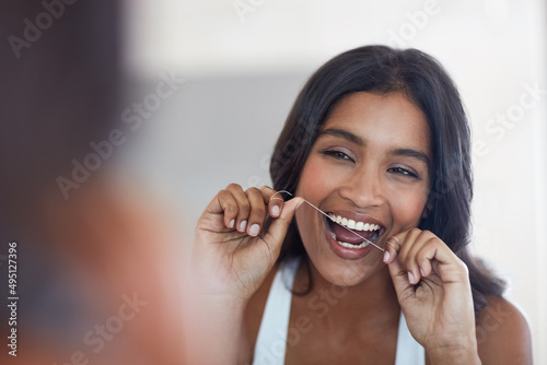 Your teeth say a lot about your health. Shot of an attractive and happy young woman flossing her teeth in the bathroom at home.