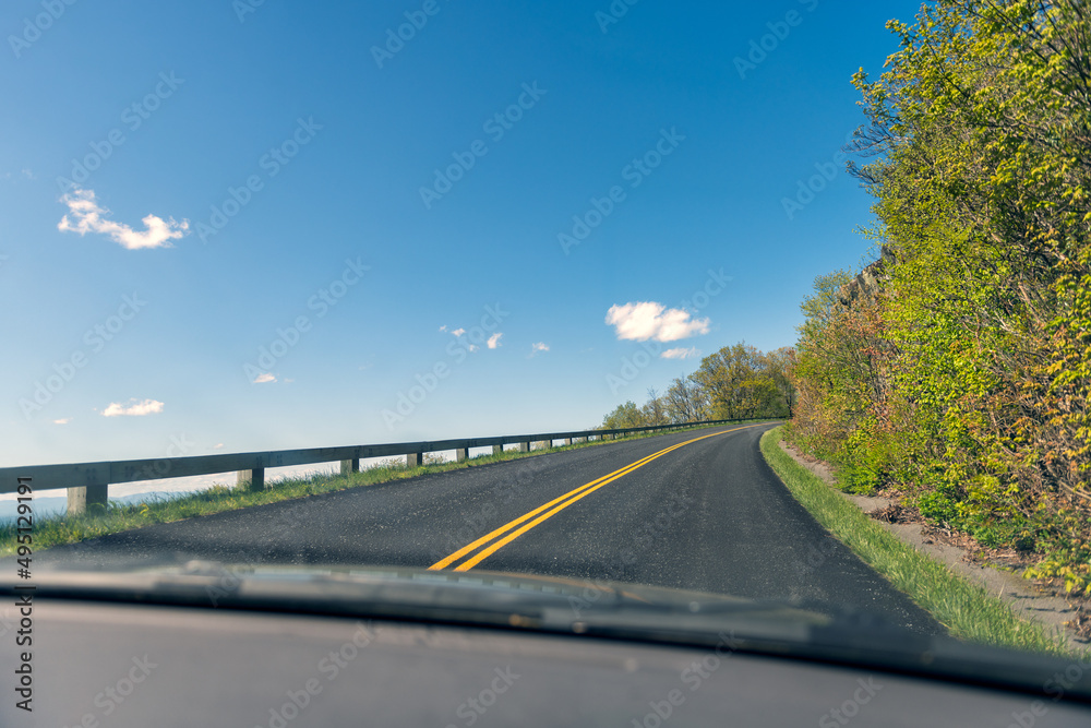 Fototapeta premium Car pov point of view driving on winding road through windshield in Blue Ridge mountains parkway in Virginia with paved asphalt road and blue sky