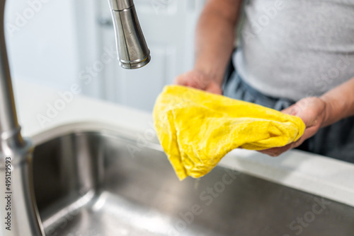 New modern gooseneck faucet tap and kitchen sink closeup on island with quartz countertops and man person cleaning washing using yellow towel