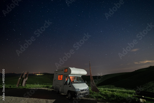 Night sky in the cultivated hill range and cereal crop fields of Tuscany, Italy. Stars over camper van illuminated by moon light. Toscana, Italia.