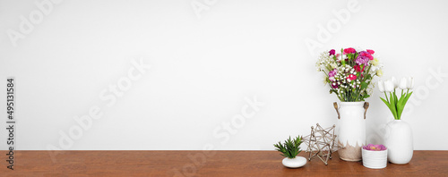 Home decor on a wood shelf. Succulent plants and vases of flowers against a white wall. Banner with copy space.