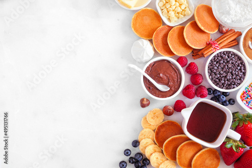 Breakfast or brunch pancake buffet side border. Top view on a white marble background. Mini pancakes with a variety of toppings.