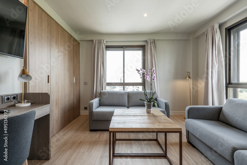 Living room with two two-seater fabric sofas  wood and metal coffee table  wooden desk with chair and large windows with curtains